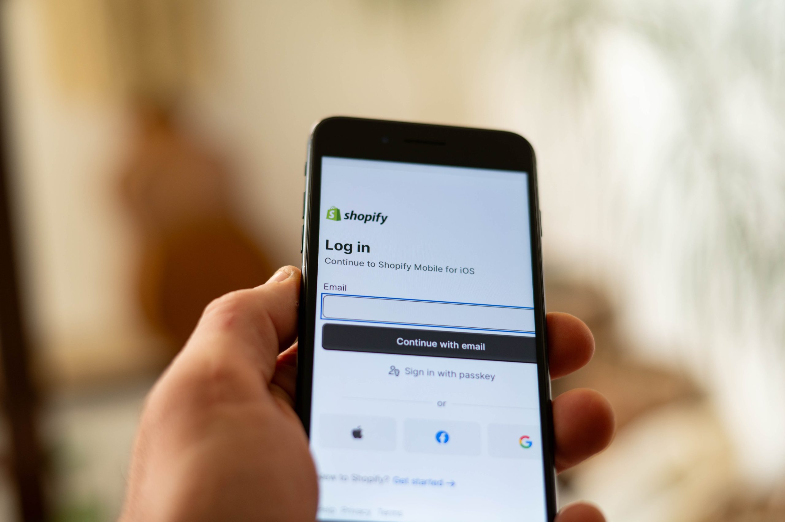 Persona holding a smartphone showing the Shopify login screen with options to sign in using email or other accounts.